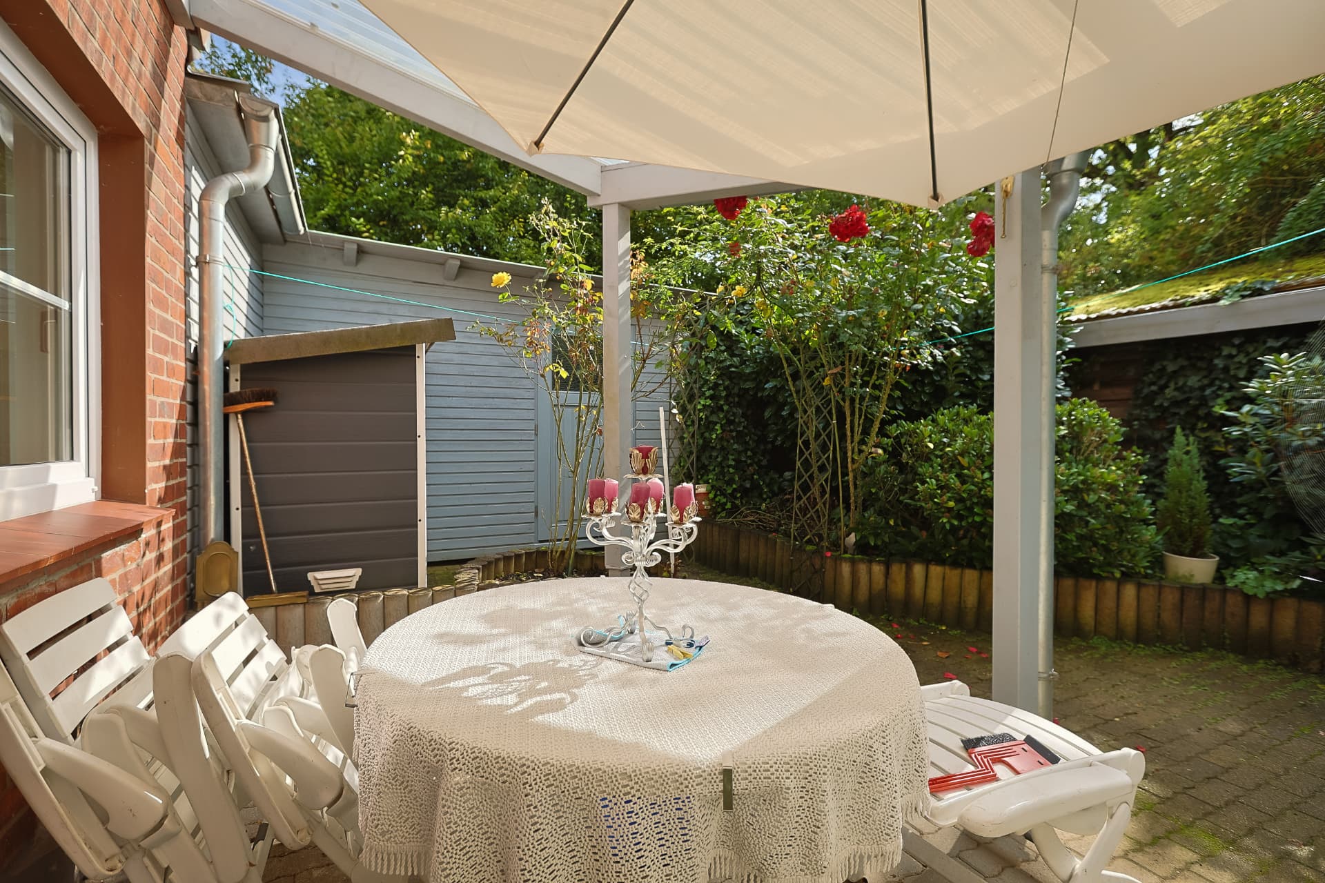 Überdachte Terrasse mit Sonnenschirm, Gartentisch und Rosen