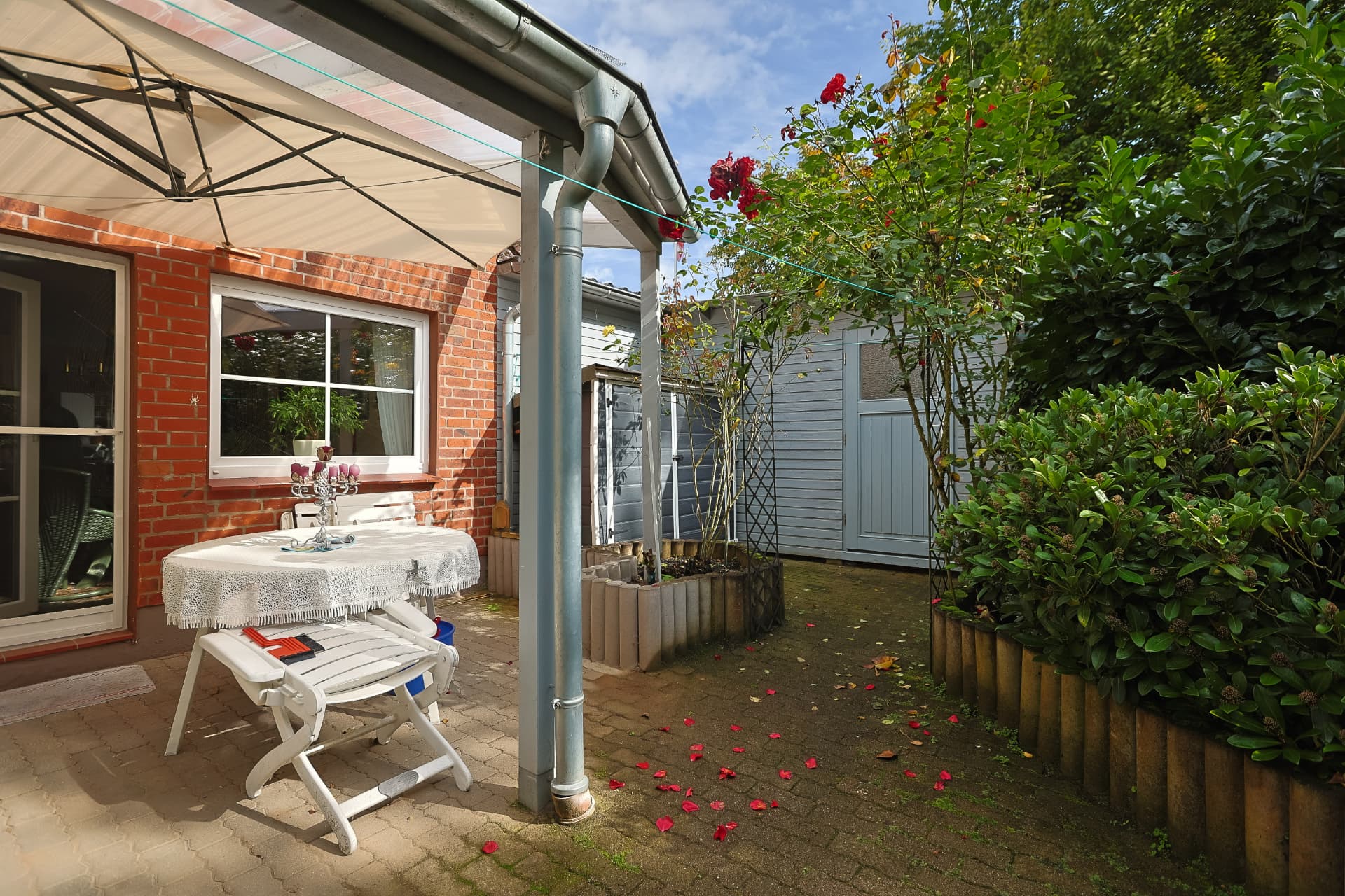 Terrasse mit Blick auf Gartenhaus, Geräteschuppen und blühenden Rosen